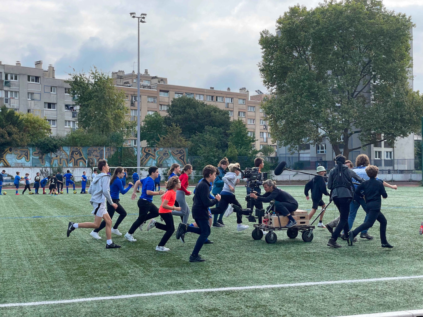 Les élèves courent sur un terrain de sport (extérieur) filmés et suivis par l'équipe technique